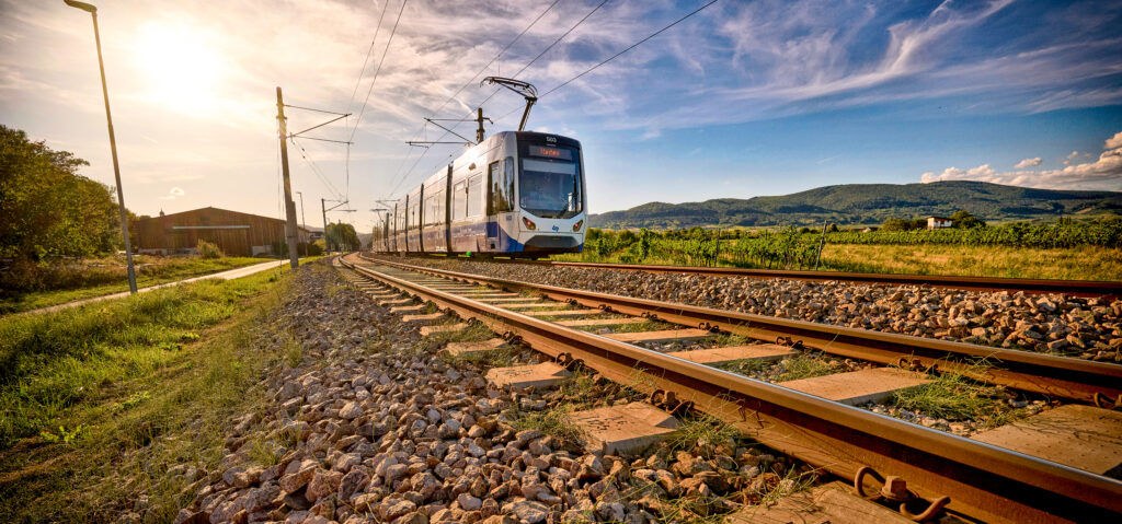 TW500 der Badner Bahn fährt entlang der Strecke in spätsommerlicher Landschaft